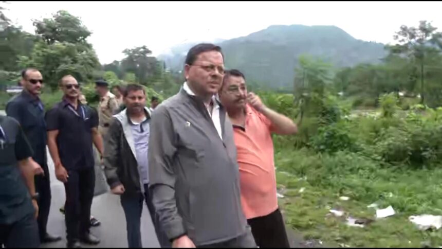 Uttarakhand CM Pushkar Singh Dhami inspecting flood-affected areas in Kesarwala, Dehradun after heavy rainfall, with damaged roads, submerged temple, and affected houses in the background