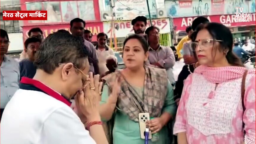 मेरठ के शास्त्री नगर में धरने पर बैठी महिला दुकानदारों के सामने हाथ जोड़ते हुए BJP नेता विनीत शारदा — जनता का दर्द और सत्ता की संवेदनहीनता का दृश्य।