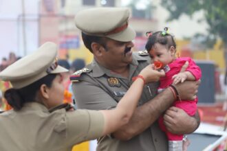 खनऊ के छठ घाट पर ड्यूटी के दौरान एक पुलिसकर्मी गोद में छोटे बच्चे को संभालते हुए, जबकि उसकी माँ पूजा कर रही है — भीड़ के बीच ममता और इंसानियत का सुंदर दृश्य।