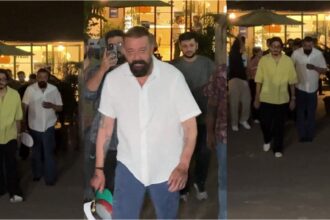 Sanjay Dutt walking in Mumbai wearing a white shirt and denim, casual confident look with night street ambience.
