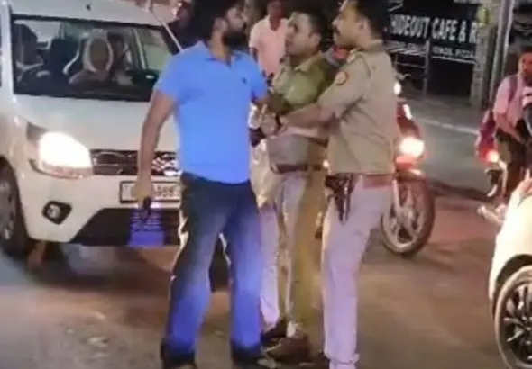 Mathura Firing Incident: Police personnel detaining a man carrying a licensed revolver after a firing incident in Mathura's Krishna Nagar area while a crowd gathers on the road.