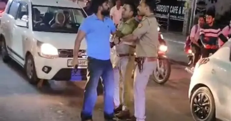 Mathura Firing Incident: Police personnel detaining a man carrying a licensed revolver after a firing incident in Mathura's Krishna Nagar area while a crowd gathers on the road.