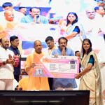 UP CM Yogi Adityanath launching the Teacher Cashless Medical Scheme at an event in Agra with education officials and beneficiaries.